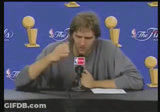 Man At Table With Microphone In Front Of NBA Trophies GIF
