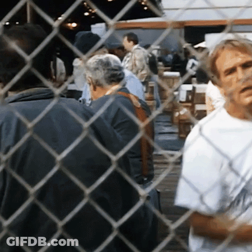 Man Behind Chain Link Fence Looking At Group GIF