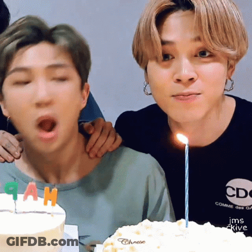 Man Blowing Out Candle On Cake While Another Man Watches GIF