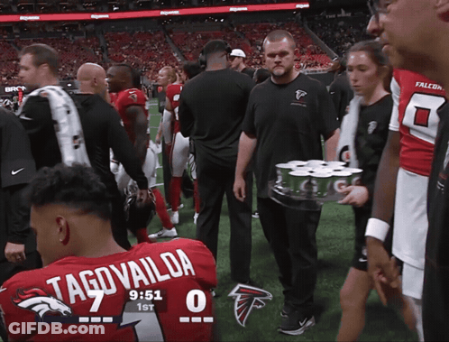 Man Carrying Beer Tray Past Man In Falcons Uniform GIF