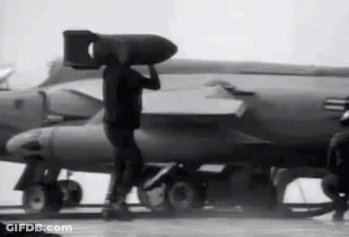 Man Carrying Large Bomb On Head In Front Of Jet GIF