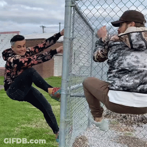 Man Climbing Chain Link Fence, Another Squats GIF