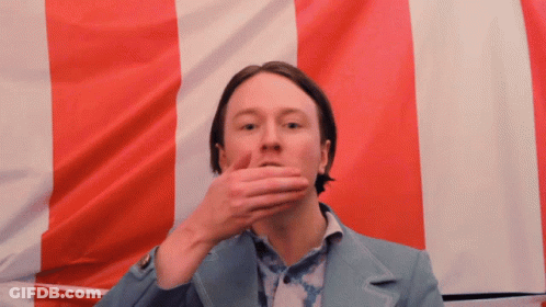 Man Covering Mouth In Front Of Red White Blue Flag GIF