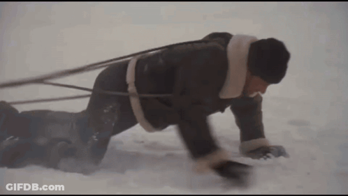 Man Crawling Through Snow Pulling Another Man On Sled GIF