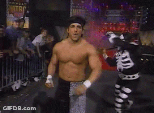Man Dancing Shirtless In Front Of Crowd With Skeleton Behind GIF