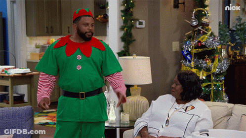 Man Dressed As Elf Standing Next To Woman On Couch GIF