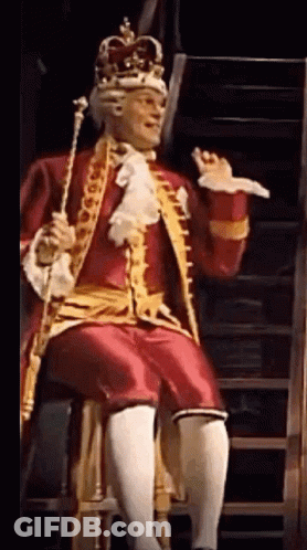 Man Dressed As King Sitting On Stool Holding Cane GIF