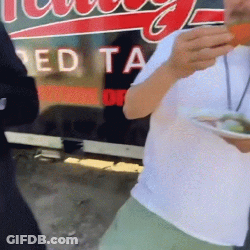 Man Eating Food In Front Of Red Ta Sign GIF