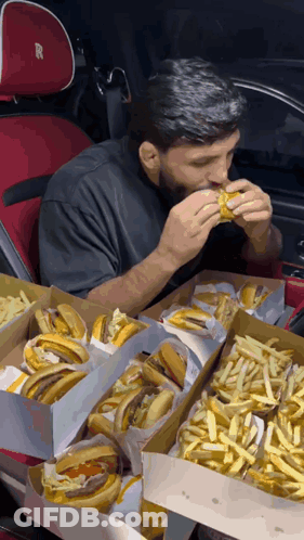 Man Eating Hamburger In Car With Boxes Of Hamburgers And French Fries GIF