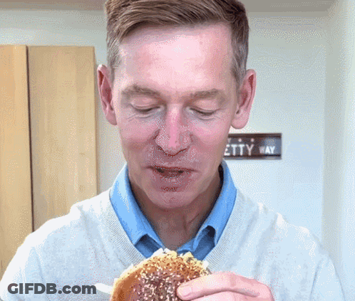 Man Eating Hamburger In Front Of Etty Way Sign GIF