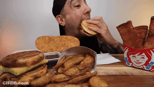 Man Eating Wendy's Sandwich Next To French Fries GIF