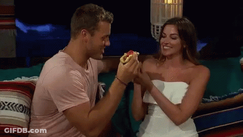 Man Feeding Hot Dog To Woman On Couch GIF