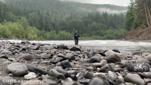 Man Fishing In River Surrounded By Rocks And Trees GIF