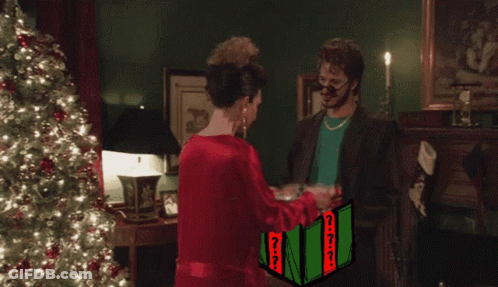 Man Giving Gift To Woman In Front Of Christmas Tree GIF