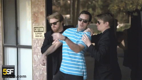 Man Held By Two Men In Front Of Caution Slippery When Wet Sign GIF