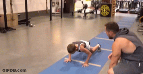 Man Helping Boy Do Push Ups On Blue Mat In Gym GIF