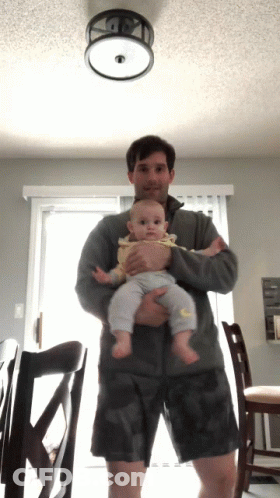 Man Holding Baby In Front Of Ceiling Light GIF