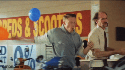 Man Holding Blue Balloon In Front Of Speeds & Scooters Sign GIF