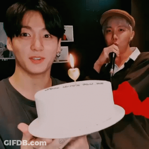 Man Holding Cake With Candle While Another Man Sings Into Microphone GIF