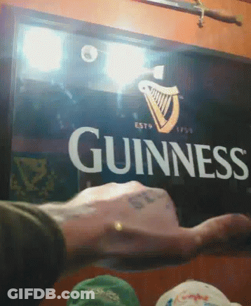Man Holding Glass In Front Of Guinness Sign GIF