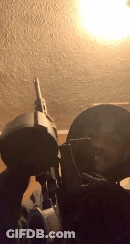 Man Holding Gun In Dark Room With Light Through Ceiling GIF