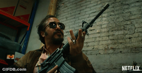 Man Holding Gun In Front Of Brick Wall With Netflix Logo GIF