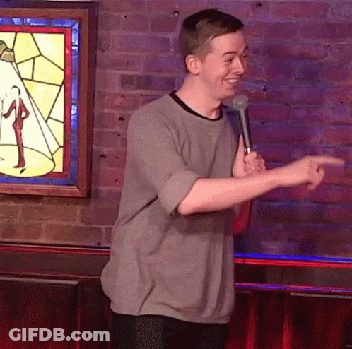 Man Holding Microphone In Front Of Brick Wall Pointing GIF