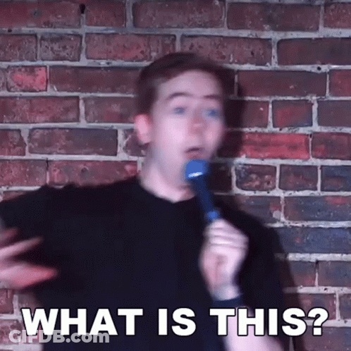 Man Holding Microphone In Front Of Brick Wall Saying What Is This GIF