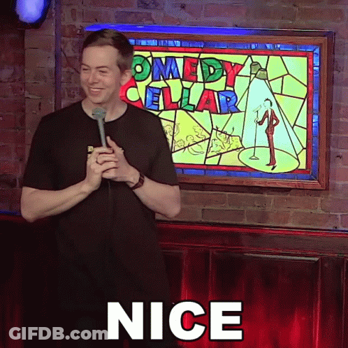 Man Holding Microphone In Front Of Comedy Cellar Sign GIF