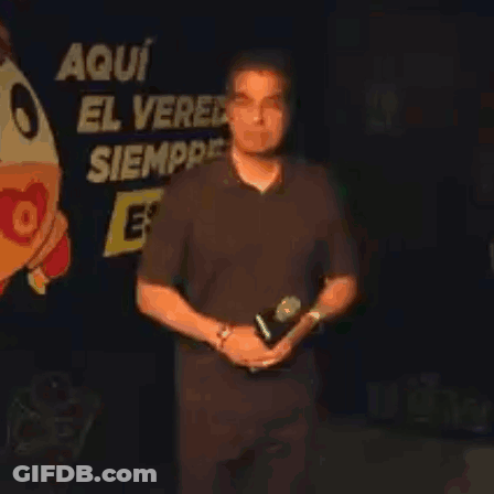 Man Holding Microphone In Front Of Sign Aqui El Ver Siempre GIF