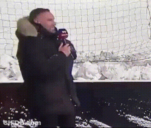 Man Holding Microphone In Front Of Snowy Fence GIF