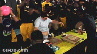 Man Holding Pizza Box Over Head In Crowded Room GIF