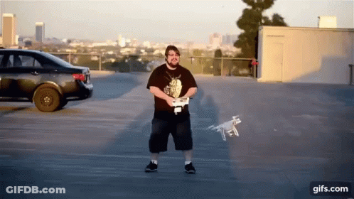 Man Holding Remote Control With Drone Flying In Parking Lot GIF