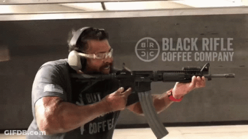 Man Holding Rifle In Front Of Black Rifle Coffee Company Logo GIF