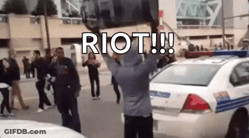 Man Holding Riot Sign In Front Of Police Car GIF