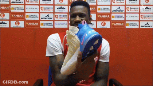 Man Holding Shoes In Front Of Ambar Wall GIF