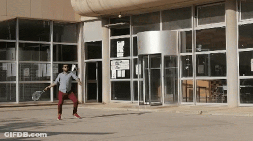 Man Holding Tennis Racquet In Front Of Building With A Sign GIF