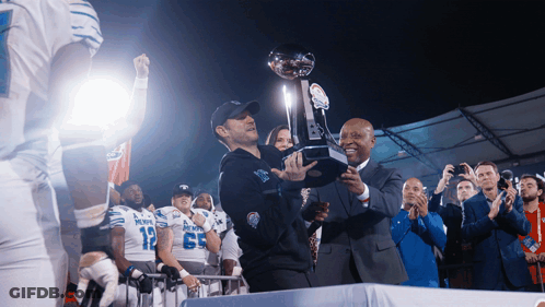 Man Holding Trophy In Front Of Denver Football Players GIF