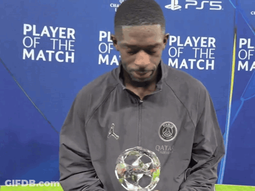Man Holding Trophy In Front Of Player Of The Match Sign GIF