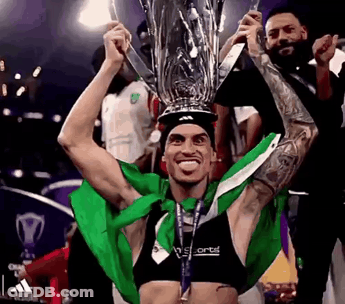 Man Holding Trophy Over Head In Green And White Shirt GIF