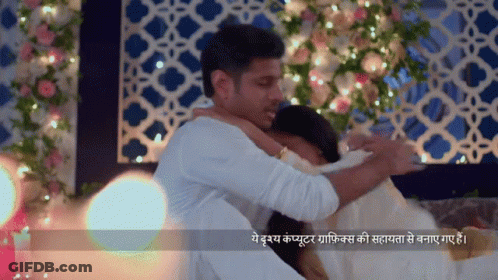 Man Hugging Woman In Front Of Flower Wall With Lights GIF