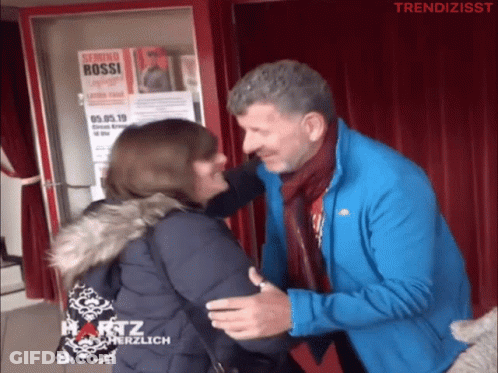 Man Hugging Woman In Front Of Serimo Bossi Sign GIF