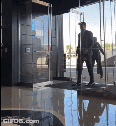 Man In A Suit Walks Through Emergency Exit Glass Door GIF
