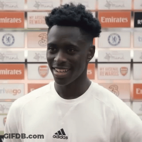 Man In Adidas Shirt Smiling In Front Of Emirates Ads GIF