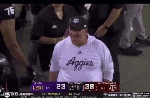 Man In Aggies Shirt In Front Of Scoreboard During Football Game GIF