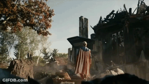 Man In American Flag Cape Standing By Destroyed House GIF