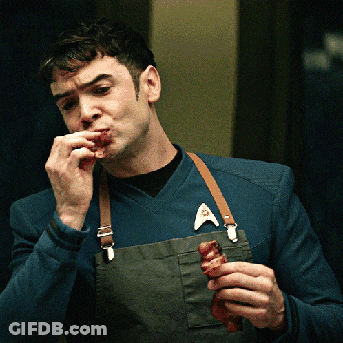 Man In Apron And Star Trek Badge Eating Meat GIF