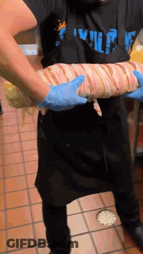 Man In Apron Holding Bacon Wrapped Meat GIF
