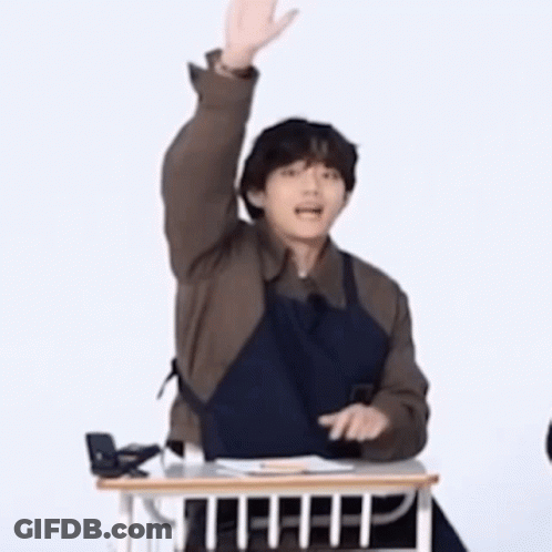 Man In Apron Sitting At Desk With Hand Up GIF