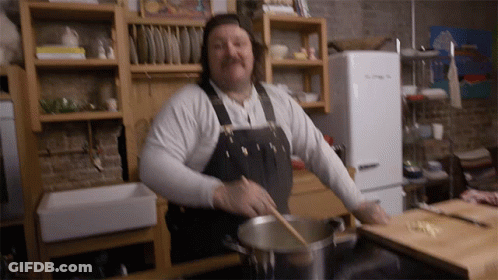 Man In Apron Stirring Pot With Wooden Spoon In Kitchen GIF